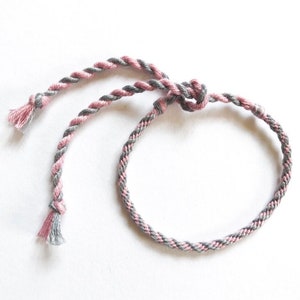 Puede incluir: Un brazalete de amistad trenzado de color rosa y gris con cierre anudado.