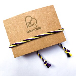 May include: A brown card with a logo of a heart with a peace sign inside and a smiley face. The text "Rahrah Crafts" is below the logo. A white, yellow, and purple cord is tied around the card.