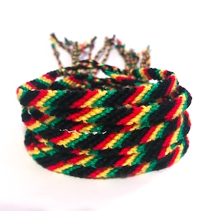 May include: A stack of colorful friendship bracelets in red, yellow, green, and black. The bracelets are woven with a diagonal pattern.