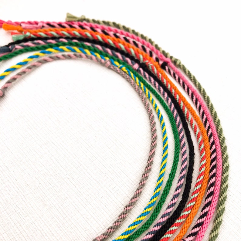 Puede incluir: Una colecci&oacute;n de cordones trenzados de colores, cada uno con un patr&oacute;n y una combinaci&oacute;n de colores diferentes. Los cordones est&aacute;n dispuestos en un semic&iacute;rculo, con los extremos de los cordones superpuestos.