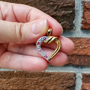 May include: A gold heart-shaped pendant with a twisted design and red and white gemstones.