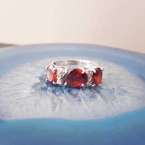 May include: A silver ring with three red gemstones and smaller white gemstones set in the band.
