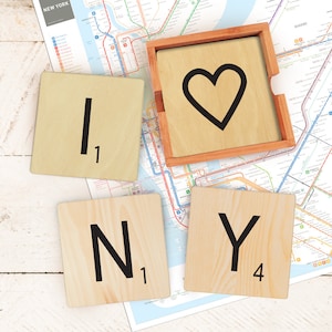 Puede incluir: Azulejos de Scrabble de madera que deletrean "I NY" con un azulejo en forma de corazón en un marco de madera. Los azulejos están sobre un mapa de la ciudad de Nueva York.