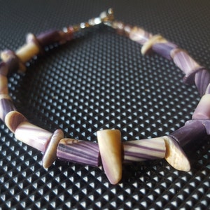 May include: A purple and white shell bracelet with a silver clasp. The bracelet is made from natural shells and is a unique and stylish accessory.