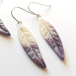 May include: A pair of silver dangle earrings with purple and white shell leaf-shaped charms.