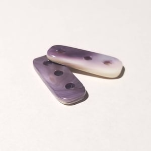 May include: Two purple and white shell buttons with four holes each.