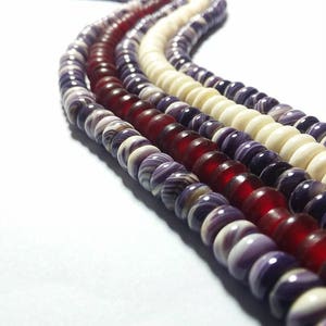May include: Three strands of beads, one white, one red, and one purple with white swirls. The beads are all round and have a smooth, polished finish.