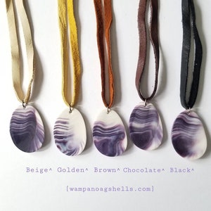 May include: Five necklaces with purple and white shell pendants on different coloured leather cords. The cords are beige, golden, brown, chocolate, and black. The text "[wampanoagshells.com]" is below the necklaces.