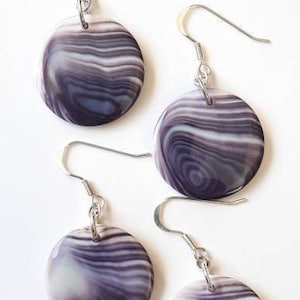May include: A pair of earrings with silver hooks and round, purple and white shell pendants.