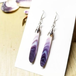 May include: A pair of dangle earrings with silver hooks and purple and white shell drops.