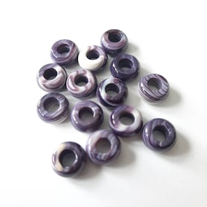 May include: A collection of purple and white shell beads with a hole in the centre. The beads are round and have a swirl pattern.