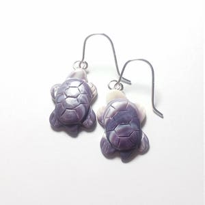 May include: A pair of silver dangle earrings featuring purple and white shell turtle charms.