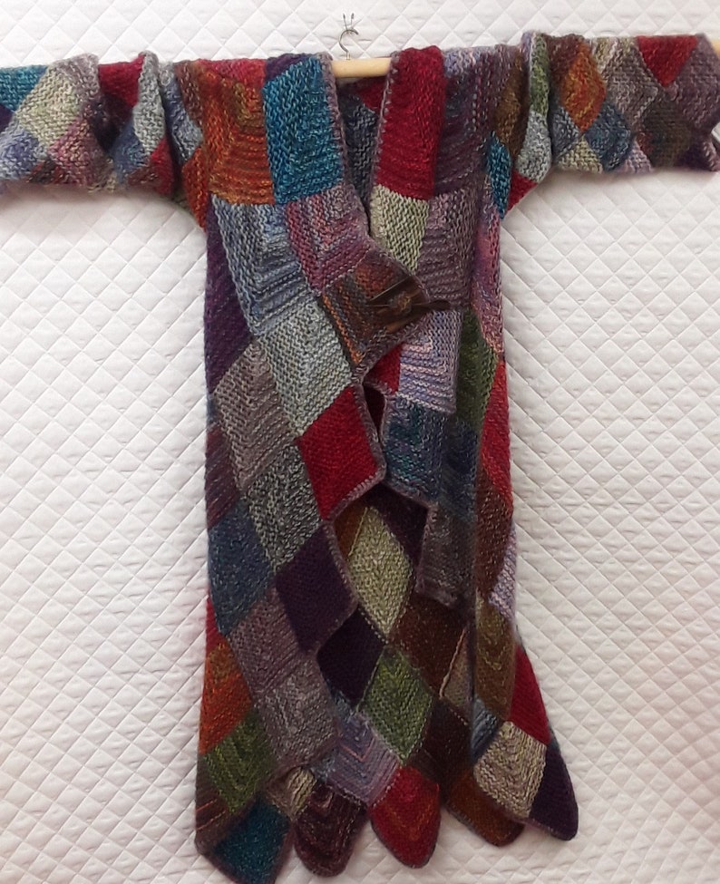 K&ouml;nnte beinhalten: Ein langer, mehrfarbiger Cardigan mit Patchwork-Muster. Der Cardigan ist aus weichem, gestricktem Stoff gefertigt und in verschiedenen Farben gehalten, darunter Rot, Blau, Gr&uuml;n, Lila und Braun. Der Cardigan ist vorne offen und hat eine lockere Passform.