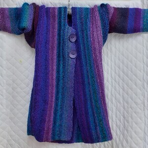 May include: A long, striped cardigan in shades of purple, blue, and teal with a button closure. The cardigan is knitted and has a relaxed fit.
