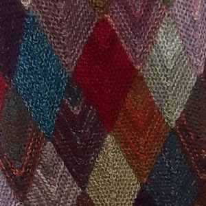 K&ouml;nnte beinhalten: Nahaufnahme eines gestrickten Stoffes mit einem Rautenmuster in den Farben Lila, Rot, Braun, Blau und Grau.