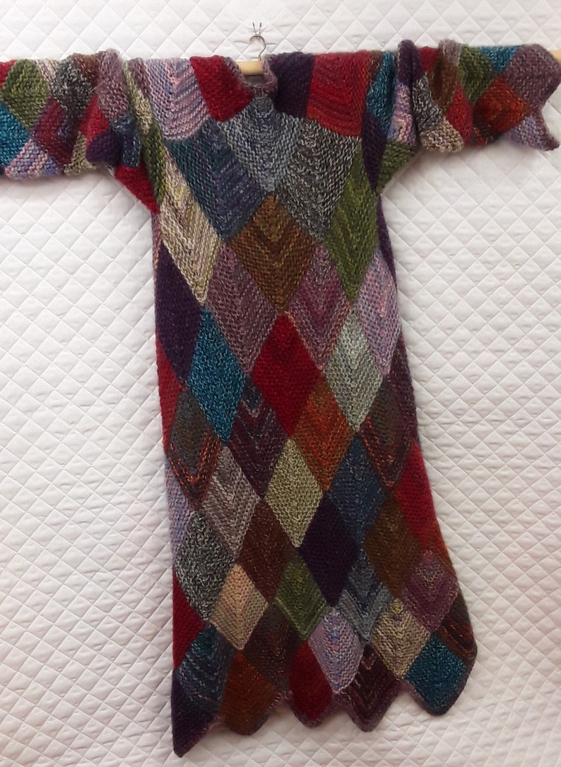 K&ouml;nnte beinhalten: Ein langer, bunter Strickpullover mit einem Rautenmuster. Der Pullover ist aus verschiedenen Farben gefertigt, darunter Rot, Blau, Gr&uuml;n und Lila.