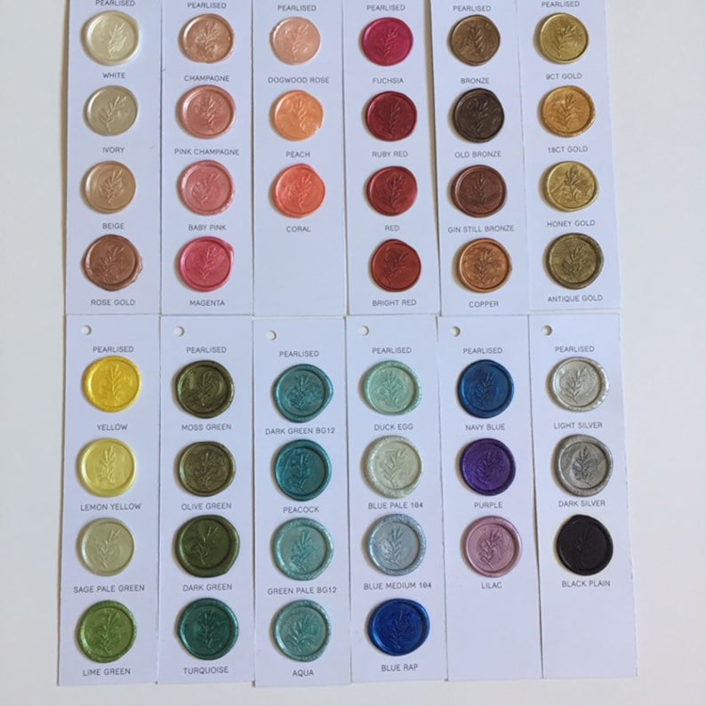 May include: A color chart of wax seal stamps with different colors and names. The chart is divided into two rows of eight columns. Each column has a wax seal stamp with a different color and name. The colors include white, champagne, dogwood rose, fuchsia, bronze, 9ct gold, ivory, pink champagne, peach, ruby red, old bronze, 18ct gold, beige, baby pink, coral, red, gin still bronze, honey gold, rose gold, magenta, bright red, antique gold, copper, yellow, moss green, dark green bg12, duck egg, navy blue, light silver, lemon yellow, olive green, peacock, blue pale 104, purple, dark silver, sage pale green, dark green, green pale bg12, blue medium 164, lilac, black plain, lime green, turquoise, aqua, and blue rap.