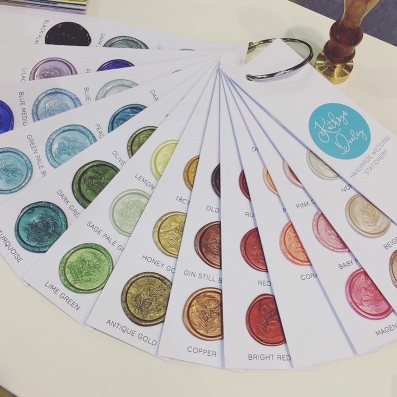 May include: A color chart of wax seal colors for wedding stationery. The chart includes a variety of colors, including turquoise, lime green, antique gold, copper, bright red, coral, baby pink, beige, and magenta. The chart also includes the text "Kithrys Duley Handmade Wedding Stationery".