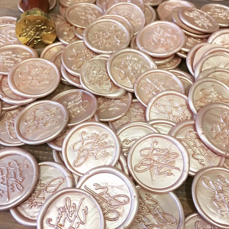 May include: A large pile of rose gold wax seals with the words "Save the Date" embossed on them.