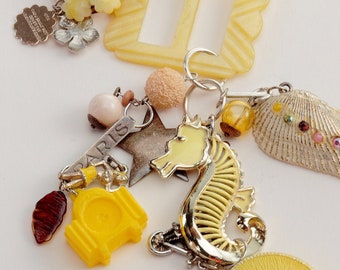 May include: A yellow and silver charm necklace with a variety of charms, including a seahorse, a star, a shell, and a button. The necklace is made with pink and yellow beads.
