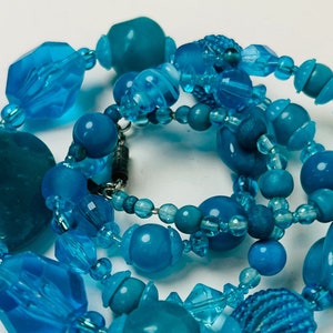 May include: A multi-strand necklace made of blue glass beads of various sizes and shapes. The necklace features a mix of round, oval, and faceted beads, creating a textured and eye-catching look.