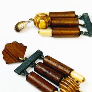 以下が含まれることがあります： 幾何学的なデザインのウッドとメタルのイヤリングのペア。イヤリングは、茶色の木製ビーズ、ゴールドのメタルアクセント、涙滴型のペンダントが特徴です。