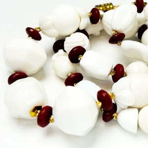 May include: A white and red beaded necklace with a variety of shapes and sizes. The beads are made of white ceramic and red glass. The necklace is strung on a gold chain.