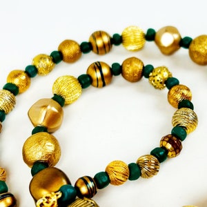 May include: A gold and green beaded necklace with a variety of different sized and textured beads. The necklace is made of gold and green beads.