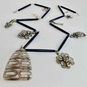 May include: A silver necklace with black beads and various silver charms, including a flower, a key, and a geometric design.