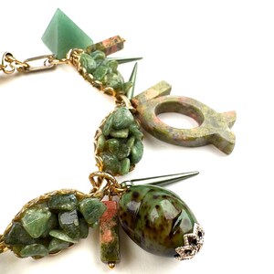 May include: A gold-toned necklace featuring various green and pink stone pendants. The necklace includes a green pyramid, a green oval stone with a silver cap, and other irregularly shaped green stone clusters. The design incorporates gold chain links and metal spikes.