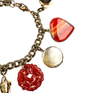 May include: A gold charm bracelet with multiple charms, including a heart-shaped charm with red agate, a round charm with a silver finish, a flower charm, and a round charm with a carved design.