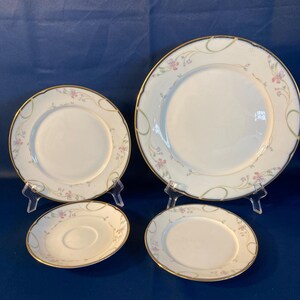 May include: A set of four white porcelain plates with a floral design and gold trim. The set includes two dinner plates and two smaller plates, likely for dessert or bread. The floral pattern features pink and green accents.