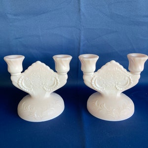 May include: Two white milk glass candle holders with a floral design. Each holder has three candle cups.
