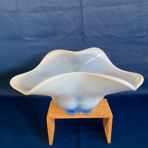 May include: A white glass bowl with a blue rim, sitting on a wooden stand. The bowl has a wavy, organic shape.