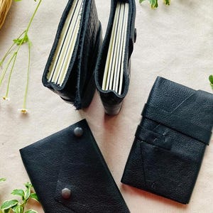 May include: Three black leather-bound journals with different sizes and styles. The journals have a rustic, handmade look and are closed.