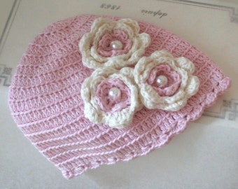 Peut inclure: Un chapeau crocheté rose avec trois fleurs crochetées blanches, chacune avec une perle en son centre.