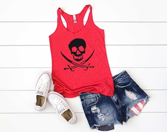 May include: Red tank top with a black skull and cross swords graphic. The tank top is laying on a white wooden surface with a pair of white sneakers and denim shorts with a red, white, and blue design.