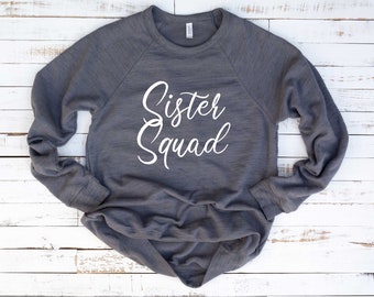 May include: A gray long-sleeved sweatshirt with the text "Sister Squad" in white cursive lettering.