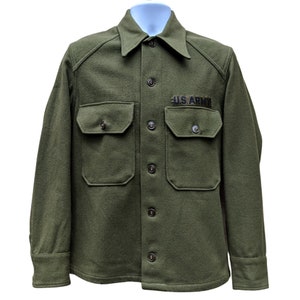 Op de afbeelding: Een groen wollen shirt met knopen en twee klepzakken. Het shirt heeft een "U.S. ARMY" patch op de rechterborst.