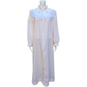 Puede incluir: Una bata de dormir larga, de color rosa acolchada, con cuello y puños de encaje blanco. La bata tiene una cremallera en la parte delantera.