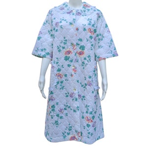 Puede incluir: Una bata acolchada blanca con estampado floral y ribete de encaje. La bata tiene un cierre de botones en la parte delantera y mangas cortas.