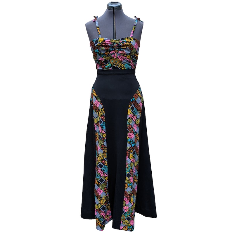 May include: A black maxi skirt with a floral print along the sides. The skirt has a fitted waist and a flowing, A-line silhouette.