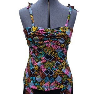 May include: A black sleeveless top with a colorful floral print. The top has a gathered bodice and thin straps that tie at the shoulders.
