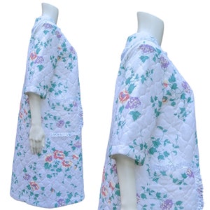 Puede incluir: Una bata blanca acolchada con estampado floral y ribete de encaje. La bata tiene mangas cortas y cuello en V.