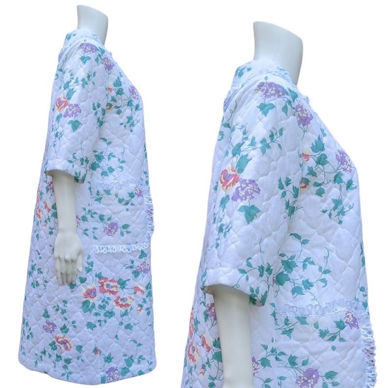 Puede incluir: Una bata blanca acolchada con estampado floral y ribete de encaje. La bata tiene mangas cortas y cuello en V.