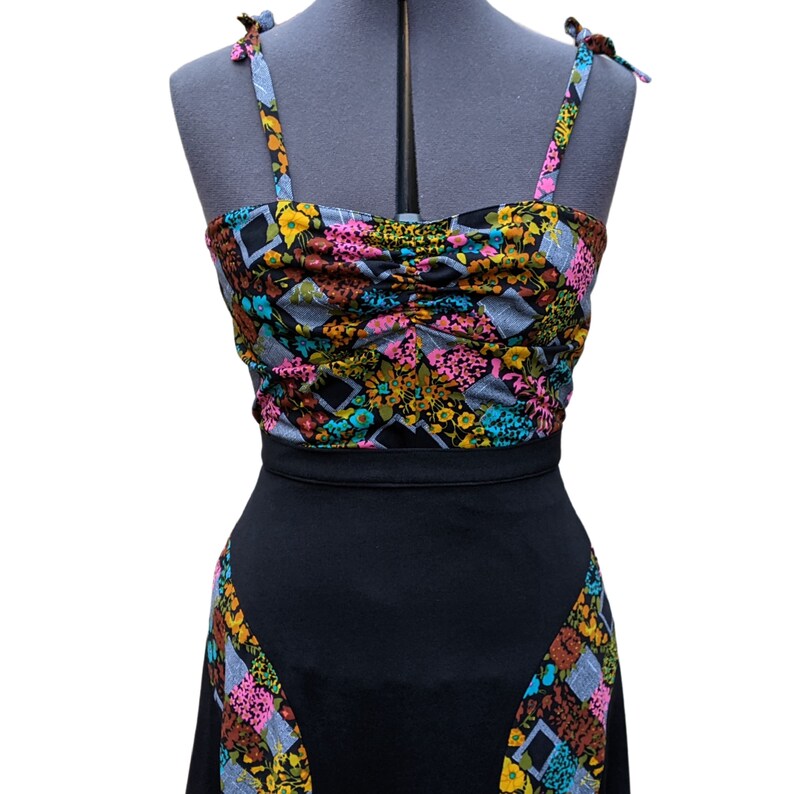 May include: A black and white dress with a floral print top and a black skirt. The top has a gathered neckline and thin straps that tie at the shoulders.