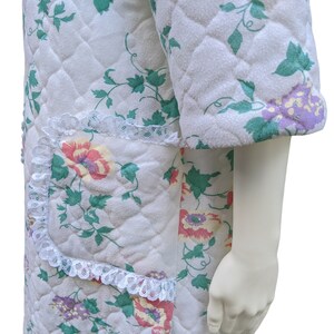 Puede incluir: Batista blanca acolchada con estampado floral y ribete de encaje. La bata tiene un bolsillo de parche en el lado izquierdo.