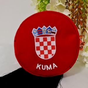 May include: Red felt circle with the Croatian coat of arms embroidered in white, blue, and red. The text "KUMA" is embroidered below the coat of arms.