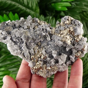 Peut inclure: Spécimen minéral naturel présentant une combinaison de pyrite, de quartz et d'autres minéraux. La pyrite est de couleur or métallique, contrastant avec les cristaux de quartz gris et transparents. Spécimen de forme irrégulière.