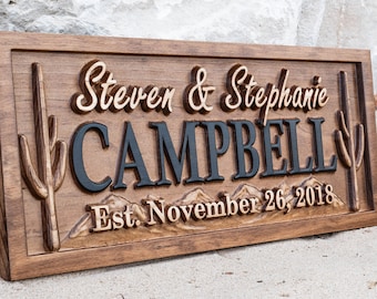 May include: A wooden sign with a carved design of mountains and cacti. The sign reads "Steven & Stephanie Campbell Est. November 26, 2018".